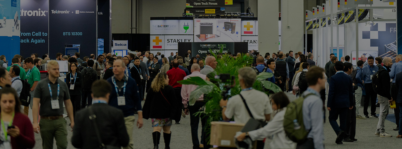 A large crowd of people walking through a bustling convention hall filled with booths and displays.