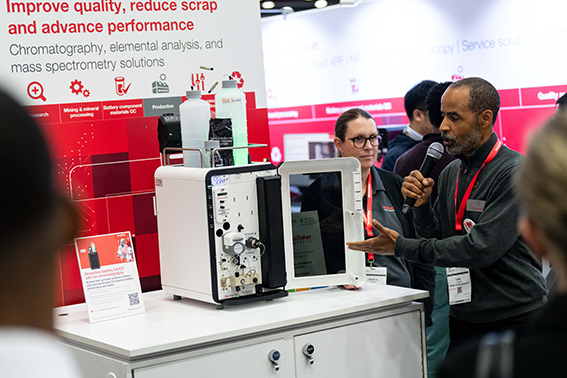 At a trade show, a man speaks with another man, amidst a lively atmosphere filled with displays and participants.