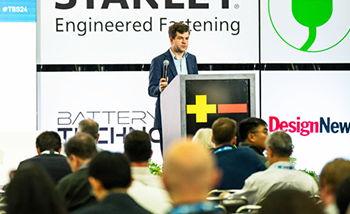 A man stands at a podium, speaking to an attentive audience at The Battery Show conference.