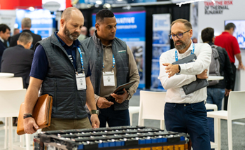 Men stand next to a large battery, examining it closely in show booth